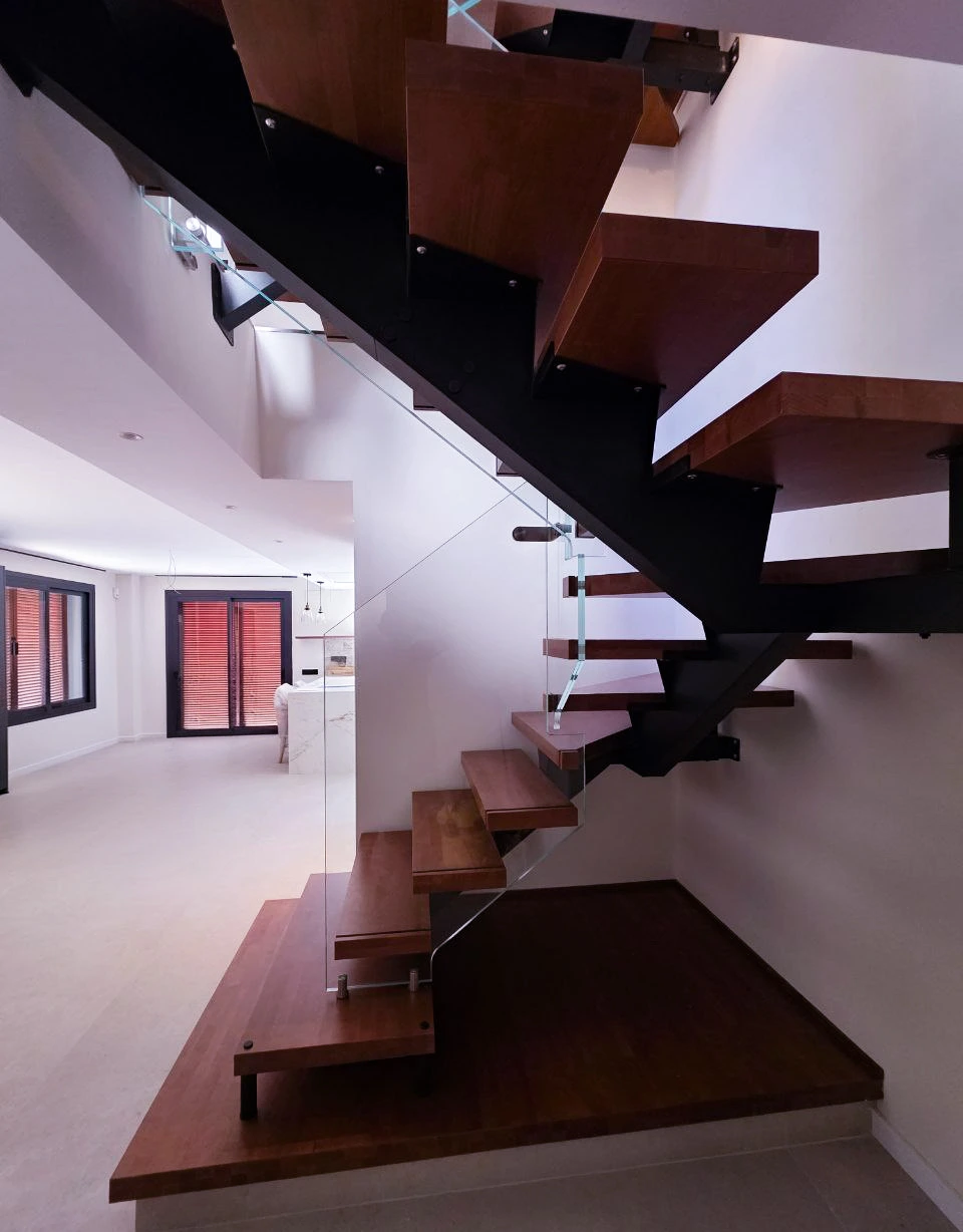 Detalle de escalera moderna con estructura metálica negra y vidrio laminado interior